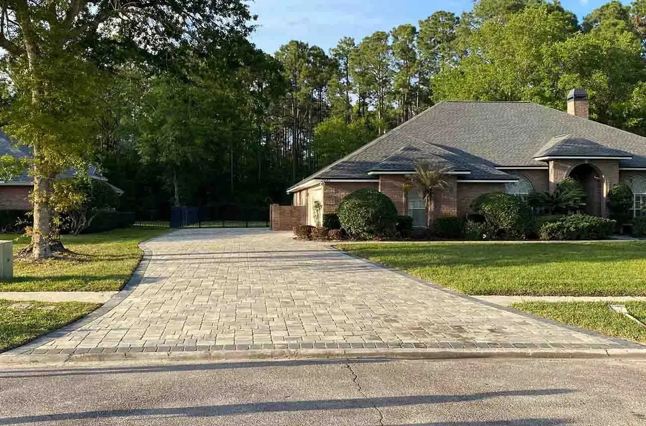 A long paver driveway curving up to a brick home among pine trees