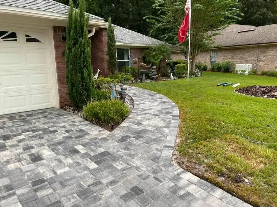 A paver walkway curving past a garage and a planting bed
