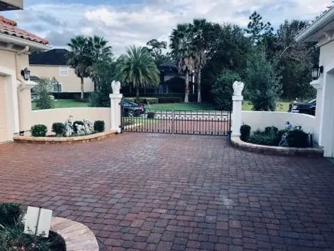 A red paver courtyard behind white gate pillars