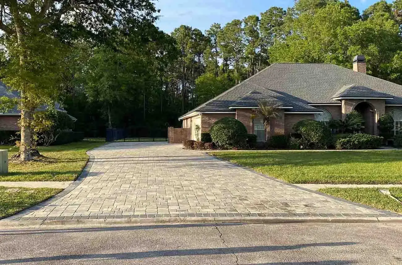 A long paver driveway curving up to a brick home among pine trees