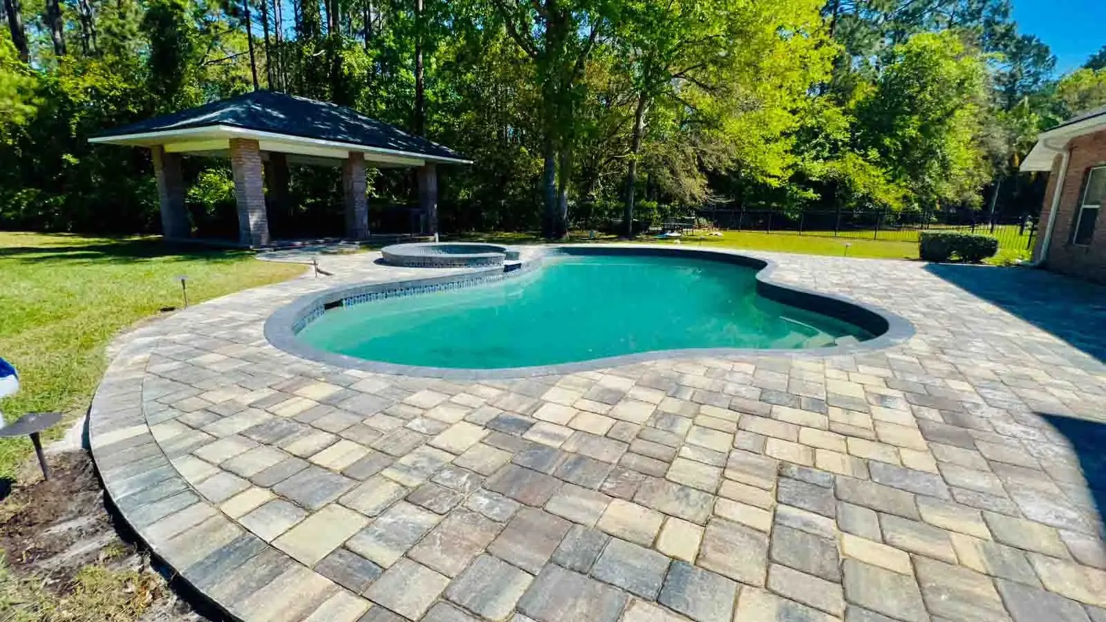 A freeform pool surrounded by a wide paver deck