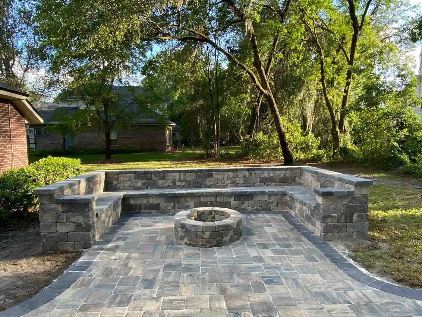 A paver patio with a round fire pit and a U-shaped seating wall