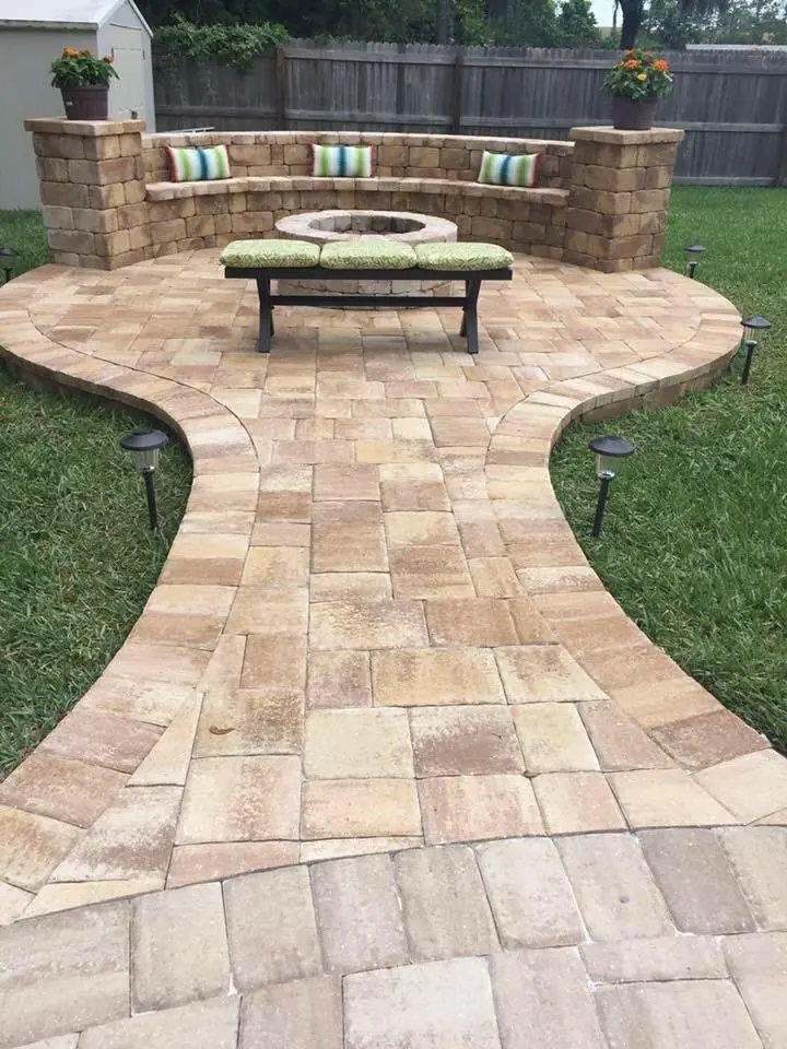 A curved paver path opening onto a round patio with a seating wall