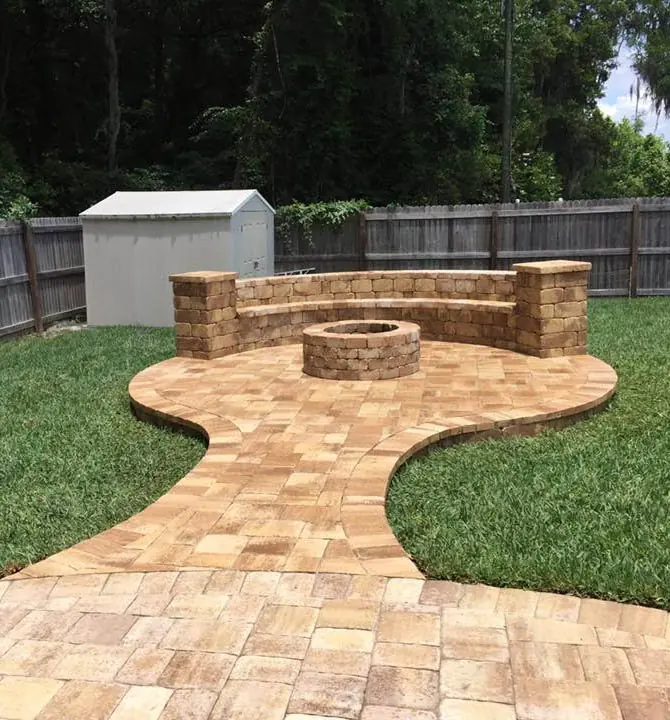 A paver path leading to a fire pit and a curved stone bench