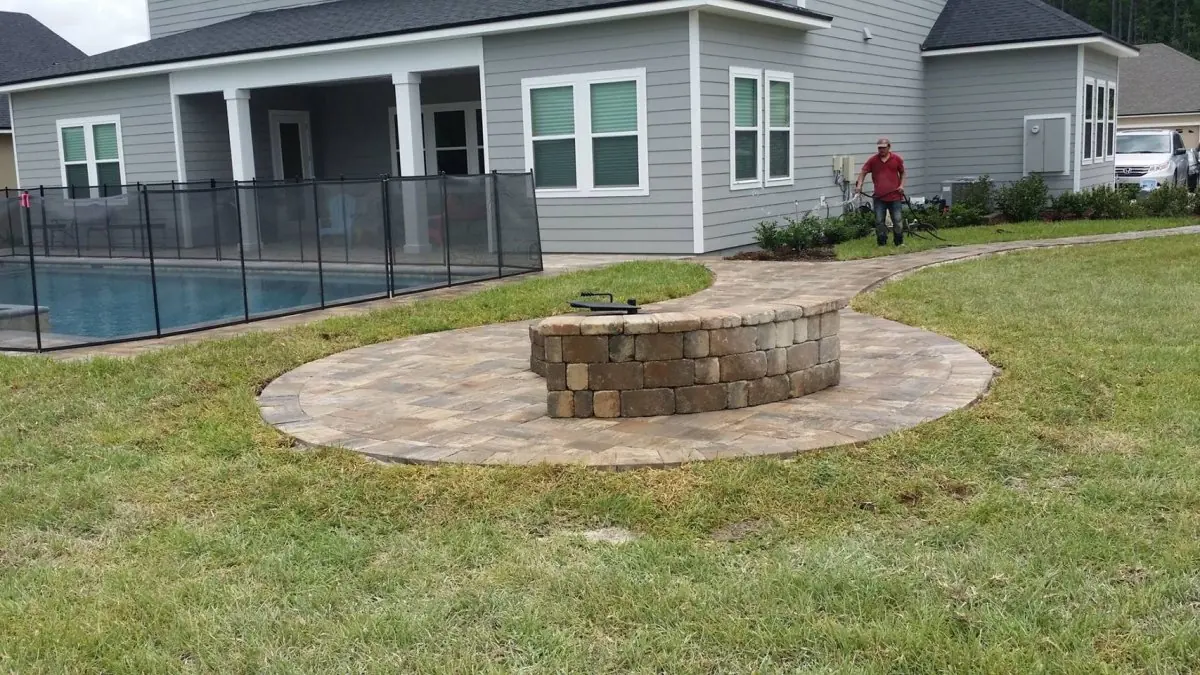 A round paver pad with a stone fire pit in a back lawn