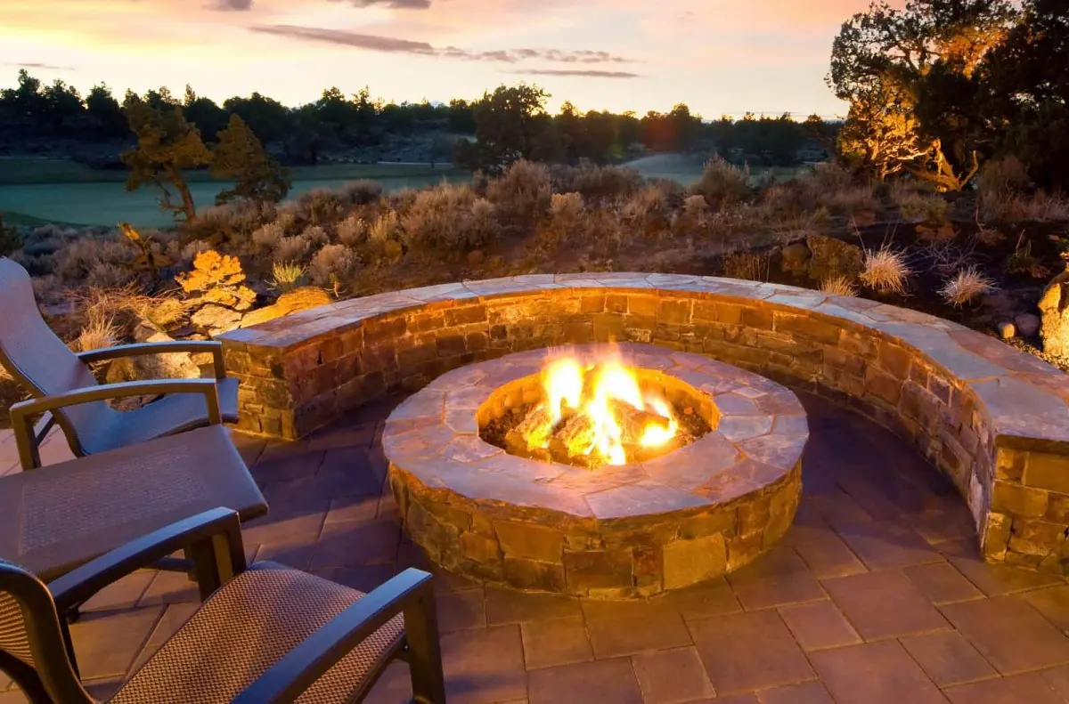 A stone fire pit burning at sunset inside a curved seating wall