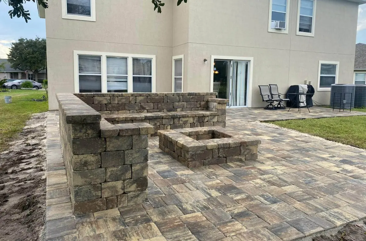 A paver patio with a square fire pit and a stone bench