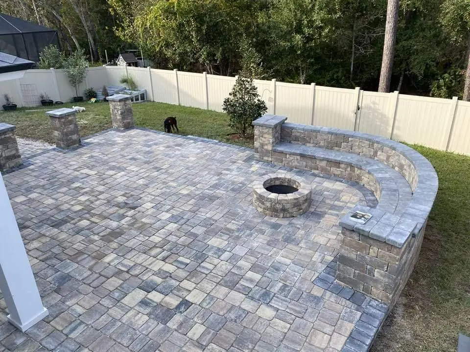 A back yard paver patio with a fire pit, pillars and a curved seating wall