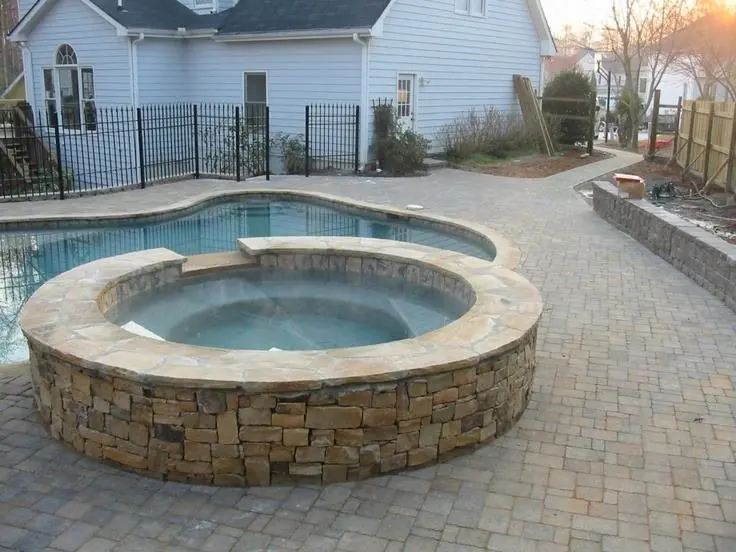A stone-faced spa beside a pool with a paver deck