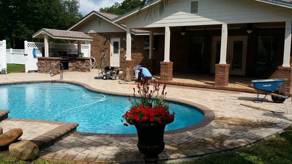 A paver deck around a freeform pool with a covered patio