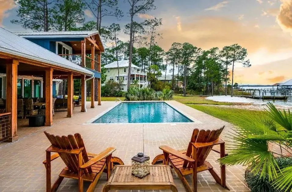 A pool deck with wooden chairs looking over the water at sunset